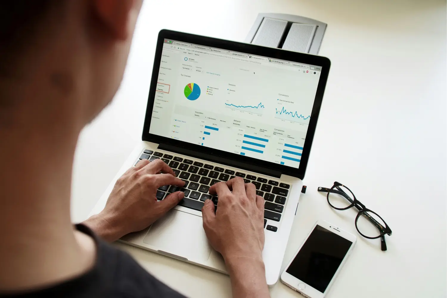 Web developer reviewing cost-effective site metrics on computer, mobile device on desk.